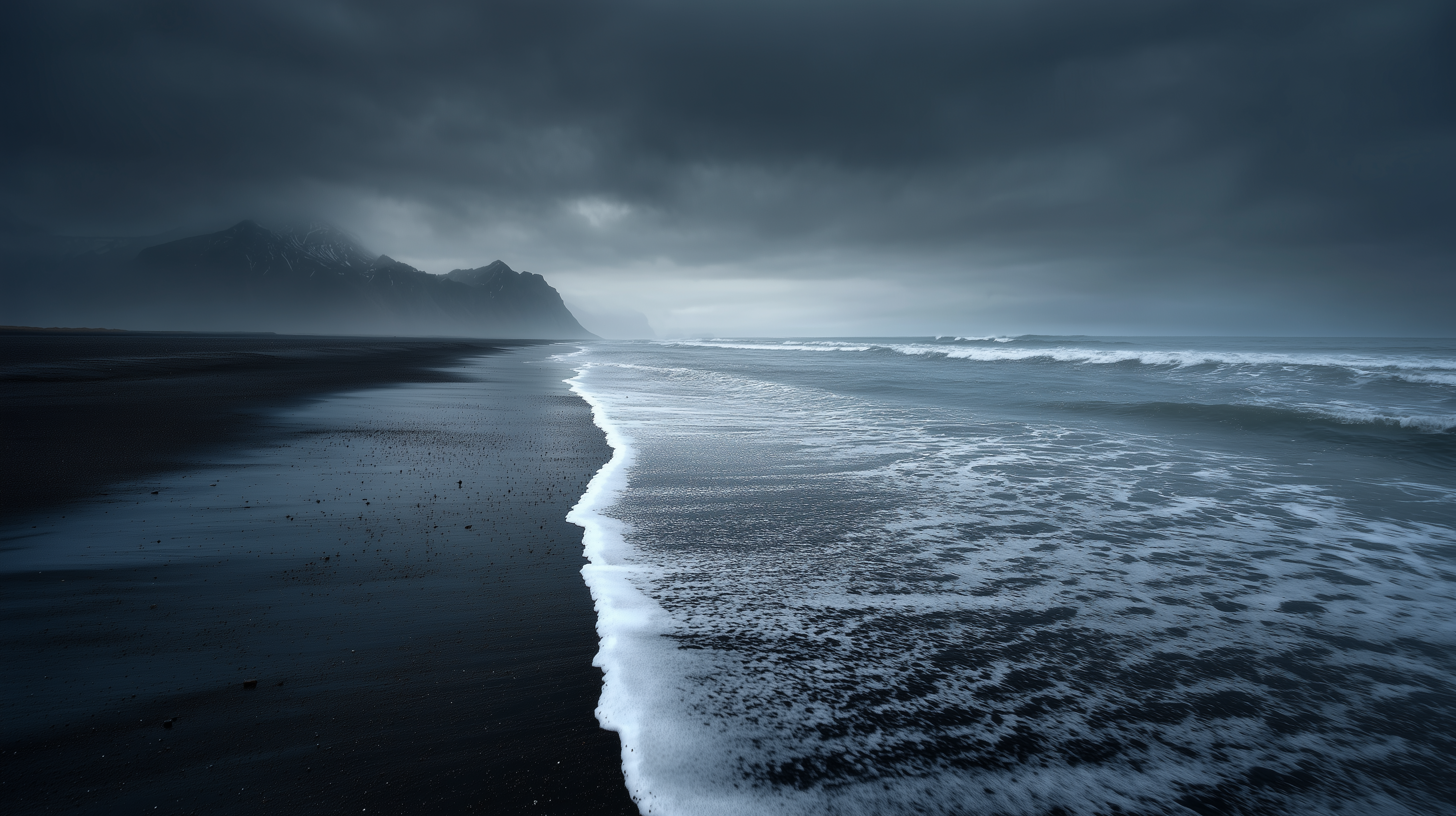 A dramatic moody seascape features dark volcanic black sand beach with white foamy waves, stormy overcast skies, and misty mountains in the distance.
